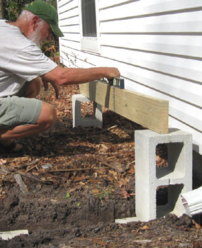 Leveling between the footings at the ends of the deck using the cinder blocks to support a piece of wood to use for the level.  Photo by Stibolt.